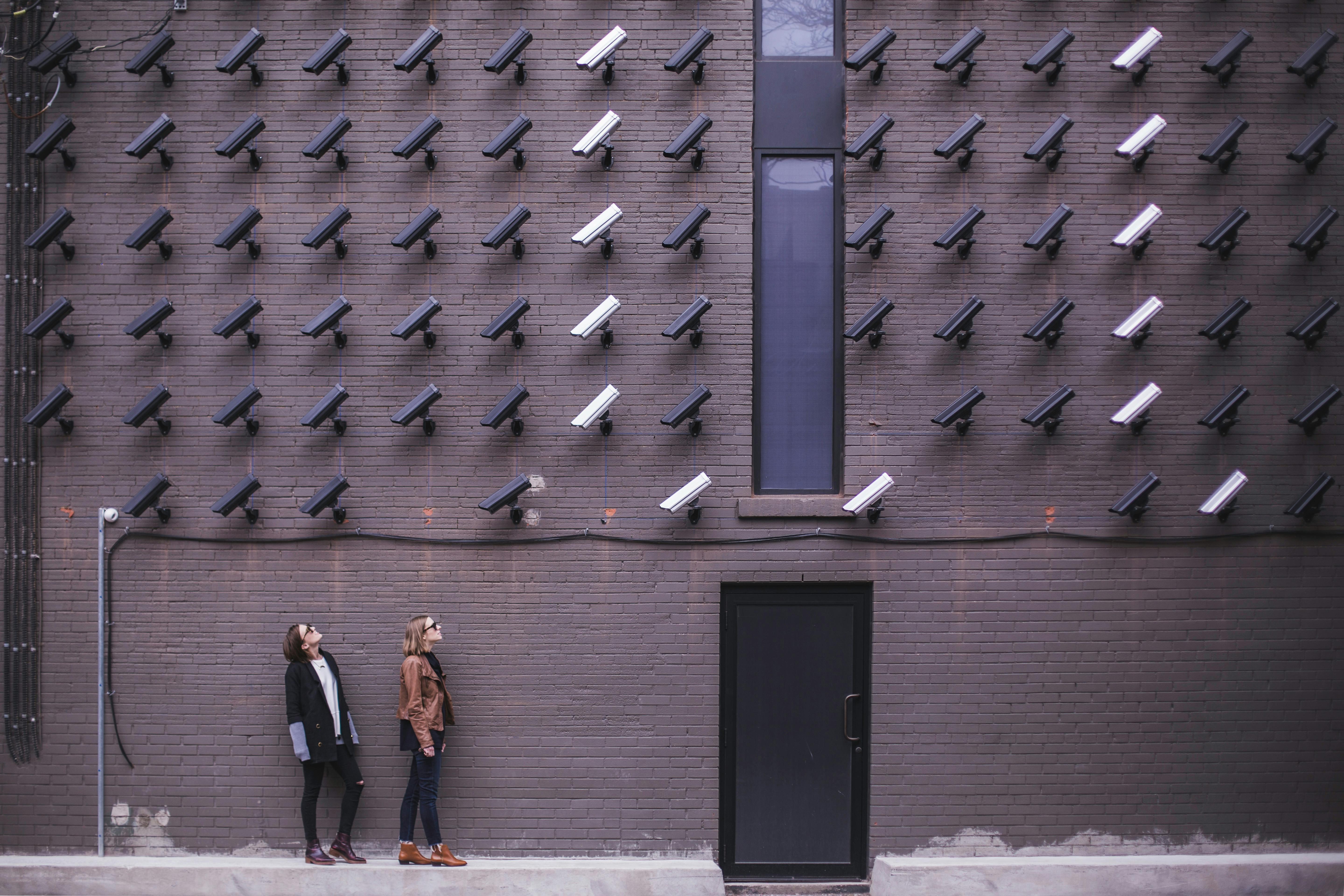 An image showing two people standing beneath a wall full of CCTV cameras.